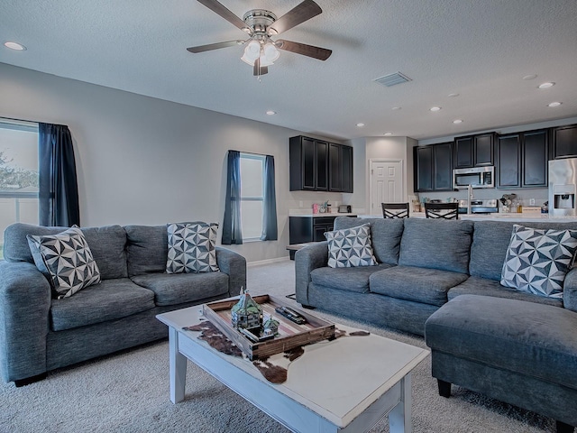 living room featuring ceiling fan, light colored carpet, and a textured ceiling