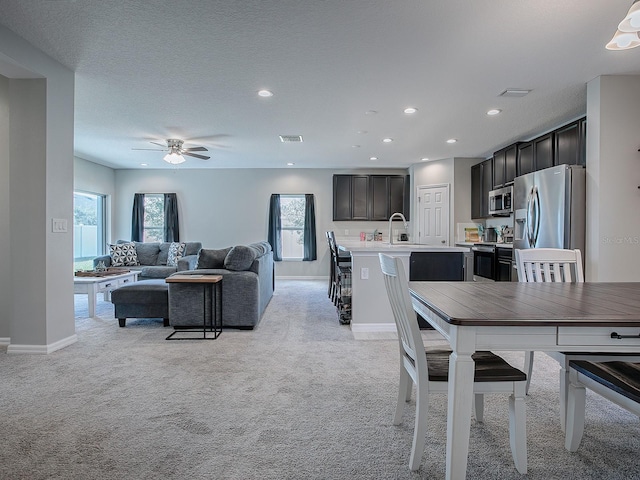 dining room with sink, ceiling fan, light colored carpet, and a textured ceiling