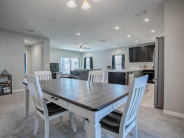 dining room with ceiling fan, sink, light colored carpet, and a textured ceiling