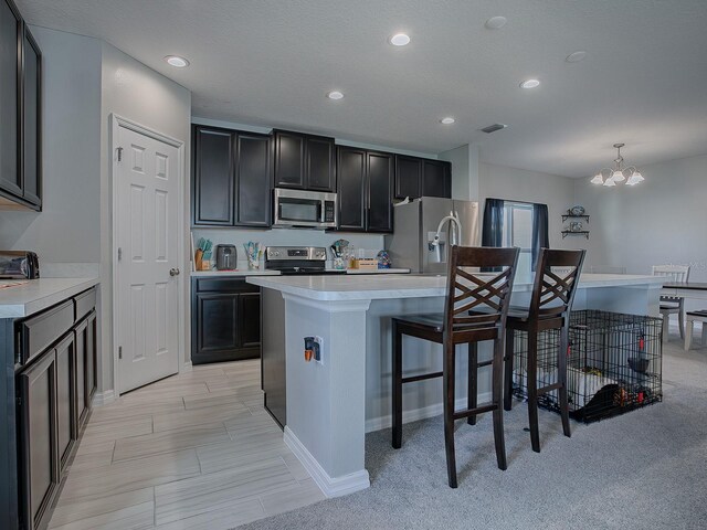 kitchen with an inviting chandelier, a center island with sink, hanging light fixtures, light colored carpet, and stainless steel appliances