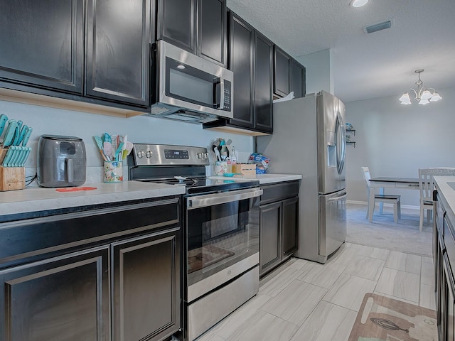 kitchen featuring appliances with stainless steel finishes, pendant lighting, a textured ceiling, and a notable chandelier