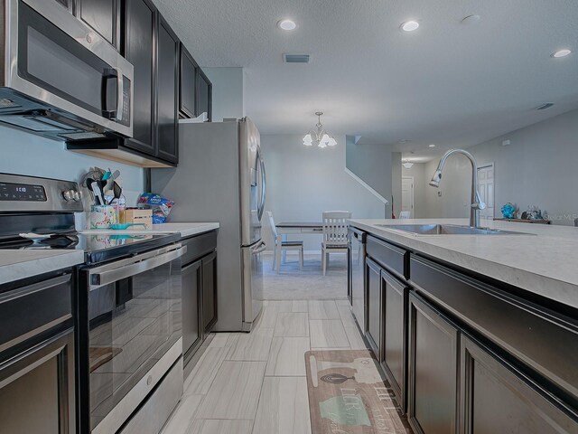 kitchen with appliances with stainless steel finishes, a textured ceiling, sink, decorative light fixtures, and a notable chandelier