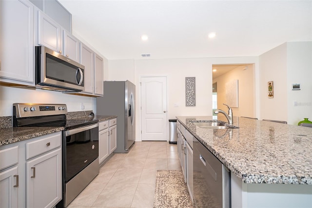 kitchen with light tile patterned floors, appliances with stainless steel finishes, an island with sink, gray cabinetry, and sink