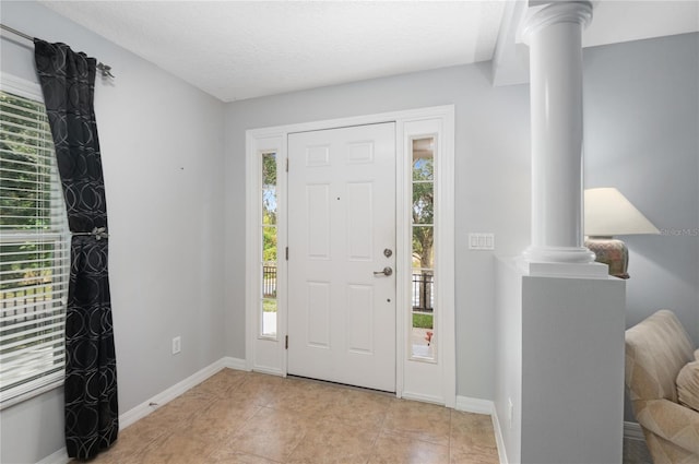 foyer featuring plenty of natural light, light tile patterned floors, and ornate columns