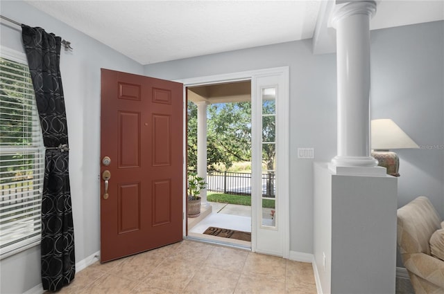 foyer entrance featuring light tile patterned floors, a textured ceiling, and decorative columns