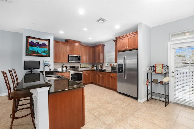 kitchen with kitchen peninsula, a kitchen breakfast bar, dark stone counters, stainless steel appliances, and sink