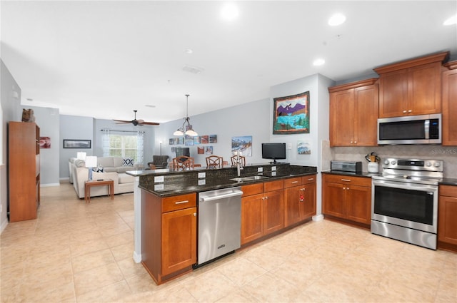 kitchen with kitchen peninsula, appliances with stainless steel finishes, dark stone counters, ceiling fan, and sink