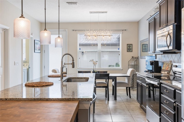 kitchen with an island with sink, hanging light fixtures, stainless steel appliances, dark stone countertops, and sink