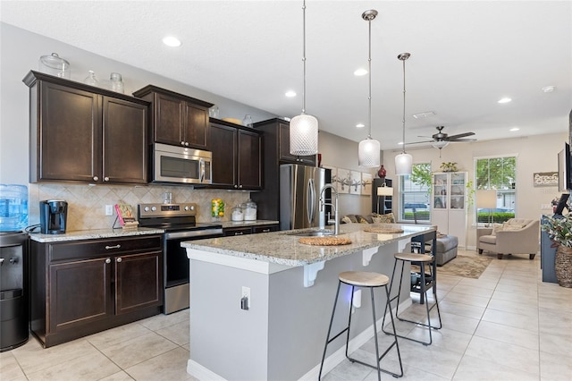 kitchen with appliances with stainless steel finishes, a sink, open floor plan, a kitchen bar, and decorative backsplash