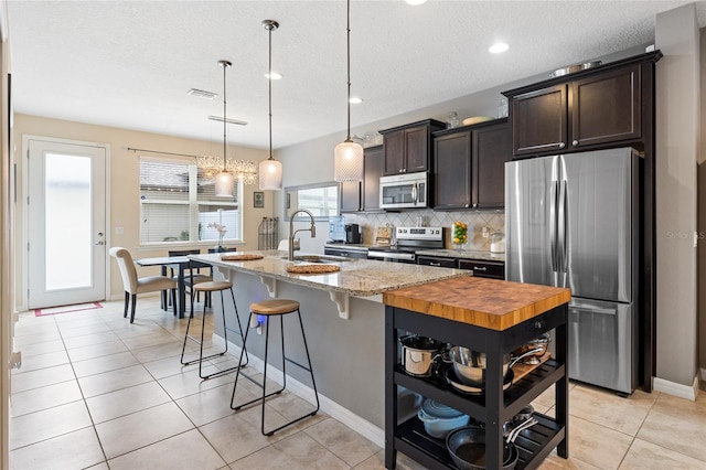 kitchen featuring light stone countertops, appliances with stainless steel finishes, sink, an island with sink, and pendant lighting