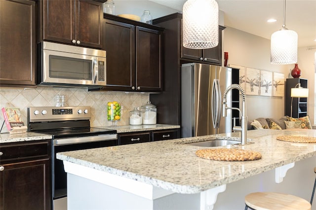 kitchen with appliances with stainless steel finishes, a center island with sink, pendant lighting, and backsplash