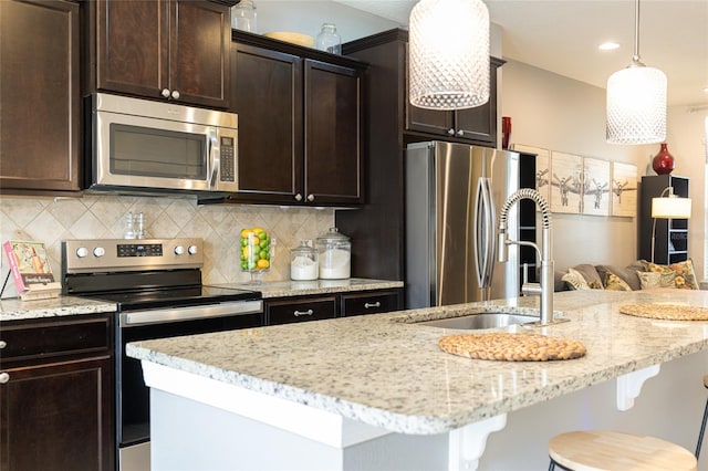 kitchen featuring stainless steel appliances, backsplash, a breakfast bar area, light stone counters, and dark brown cabinets