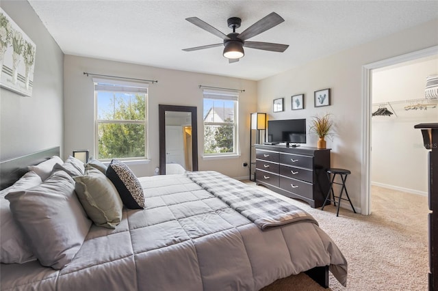 bedroom featuring carpet, a ceiling fan, a walk in closet, a textured ceiling, and baseboards