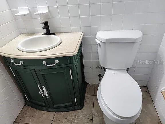 bathroom featuring vanity, toilet, and tile walls