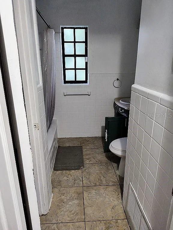 bathroom featuring toilet, shower / bath combo with shower curtain, and tile walls