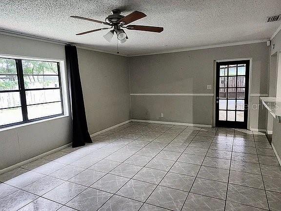 tiled empty room with ceiling fan, a textured ceiling, and ornamental molding