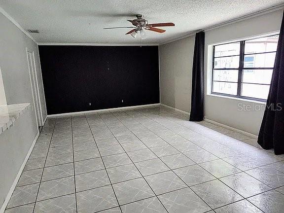 tiled spare room featuring ornamental molding, a textured ceiling, and ceiling fan