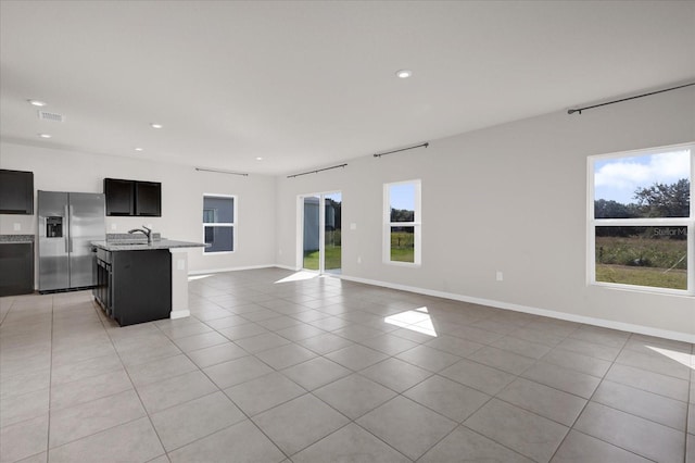 kitchen featuring stainless steel refrigerator with ice dispenser, a kitchen island with sink, a healthy amount of sunlight, and sink