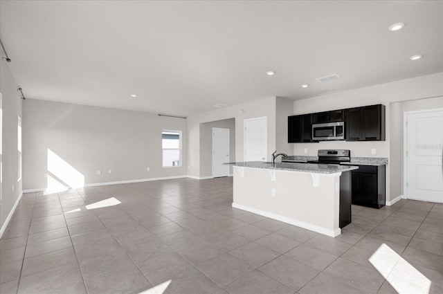 kitchen featuring light stone counters, an island with sink, a kitchen bar, light tile patterned floors, and appliances with stainless steel finishes