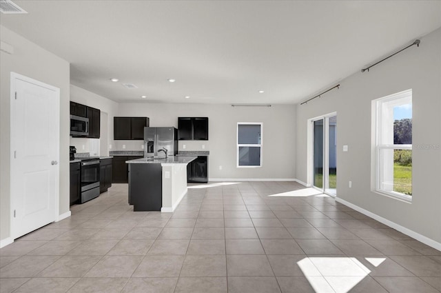 kitchen featuring light stone countertops, an island with sink, stainless steel appliances, and light tile patterned floors