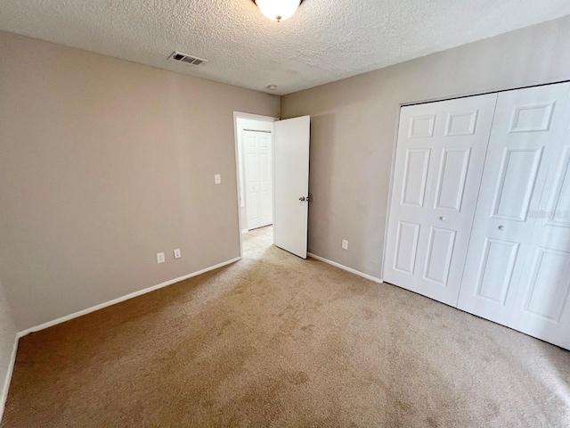 unfurnished bedroom featuring light carpet, a closet, and a textured ceiling