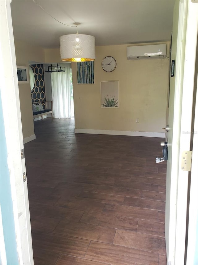 empty room featuring dark wood-style floors, a wall unit AC, and baseboards