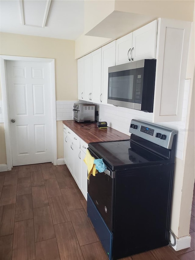 kitchen featuring electric range, white cabinets, wood counters, stainless steel microwave, and backsplash