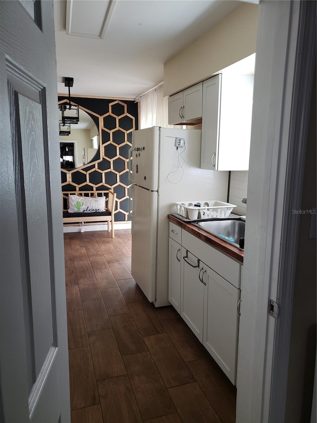 kitchen with dark wood-style flooring, freestanding refrigerator, white cabinets, a sink, and butcher block countertops