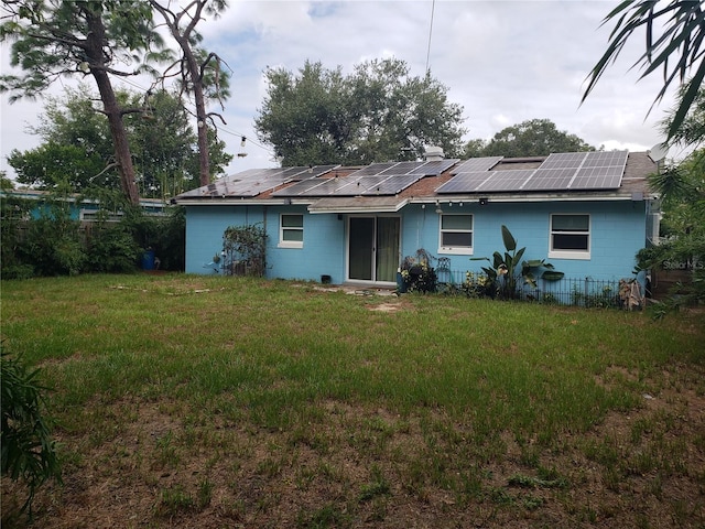 rear view of house with concrete block siding, solar panels, and a yard