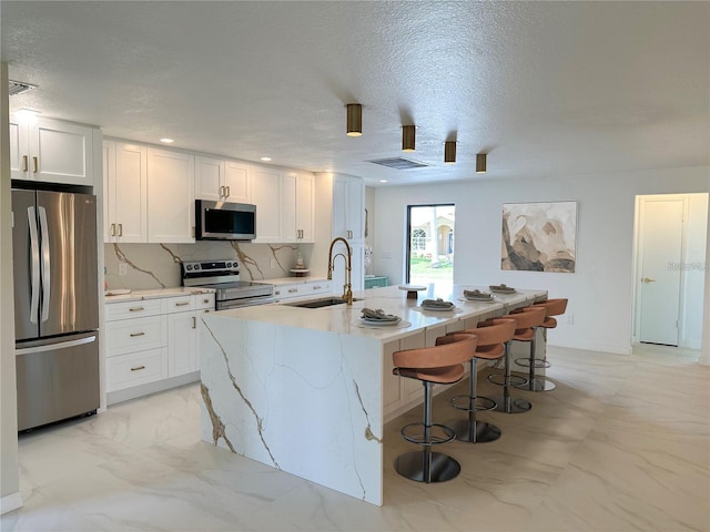 kitchen featuring stainless steel appliances, white cabinetry, sink, an island with sink, and a breakfast bar area