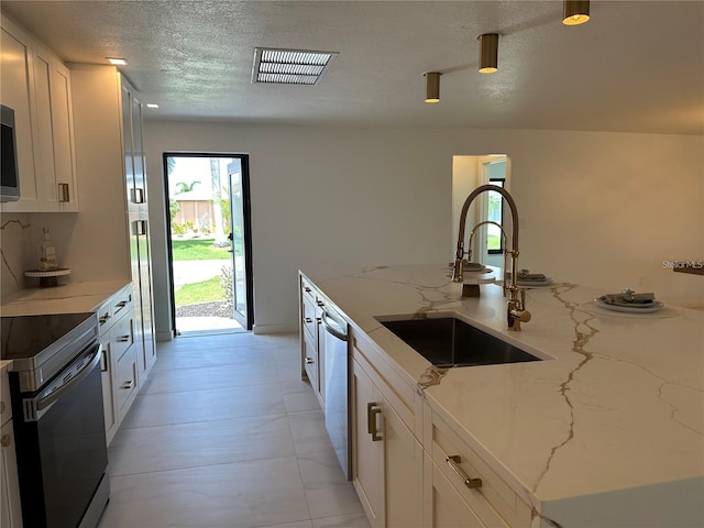 kitchen with white cabinetry, stainless steel appliances, sink, and light stone countertops