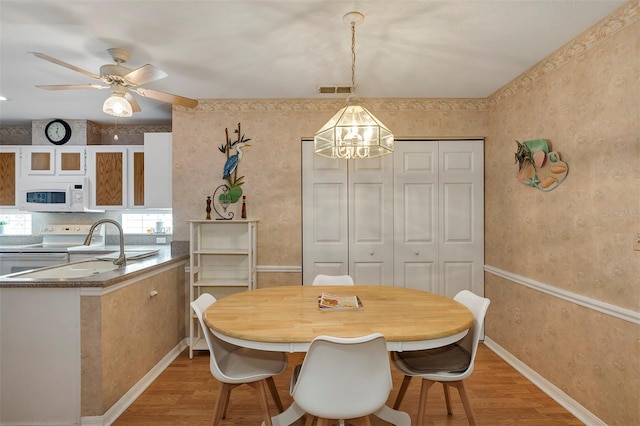 dining space with ceiling fan with notable chandelier and light wood-type flooring