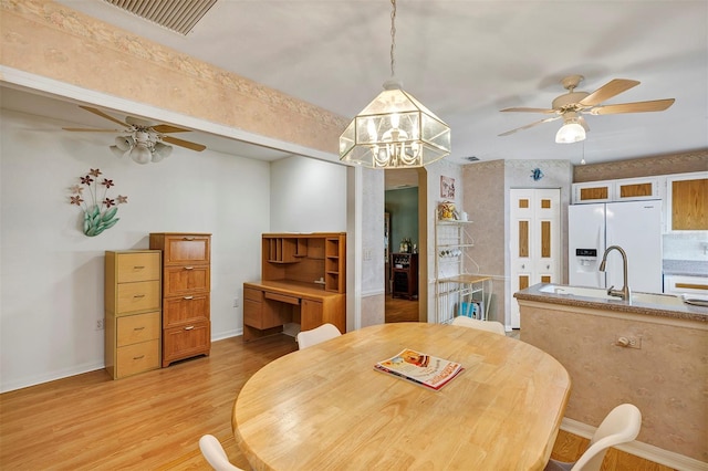 dining space with sink, ceiling fan with notable chandelier, and light wood-type flooring