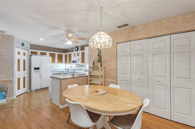 dining room with ceiling fan with notable chandelier and light wood-type flooring