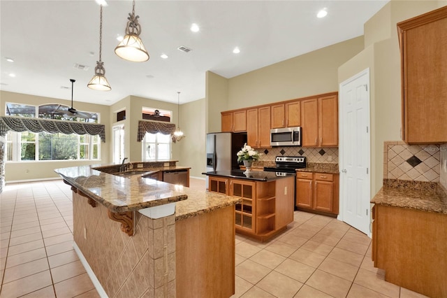 kitchen featuring appliances with stainless steel finishes, decorative light fixtures, light tile patterned floors, decorative backsplash, and an island with sink