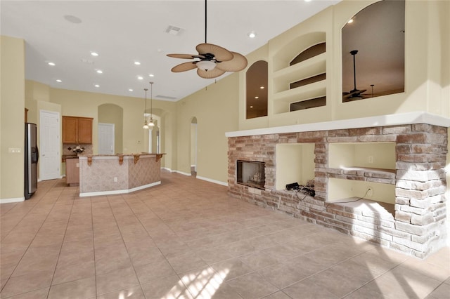 unfurnished living room featuring a stone fireplace, built in features, light tile patterned floors, and ceiling fan