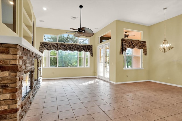 unfurnished living room featuring a stone fireplace, light tile patterned floors, and ceiling fan with notable chandelier