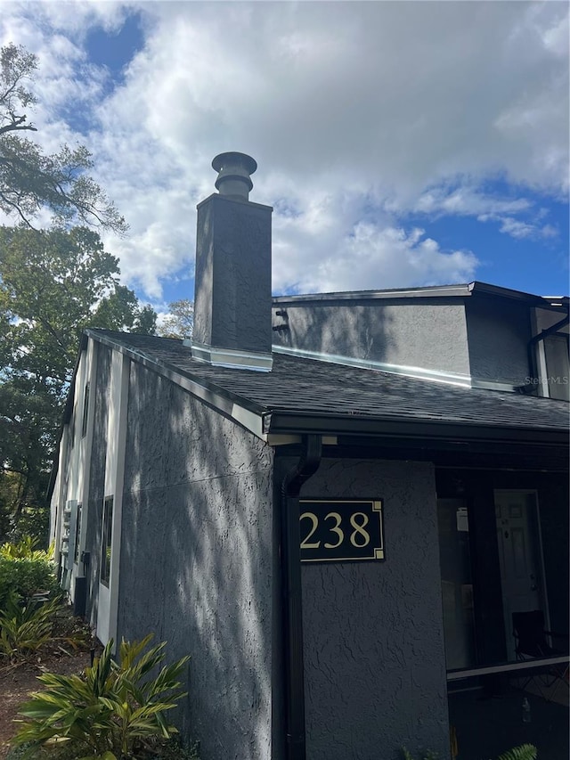 exterior space with a downspout, gutters, roof with shingles, and a chimney