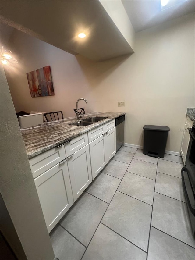 kitchen featuring dark stone countertops, sink, light tile patterned floors, stainless steel dishwasher, and white cabinetry