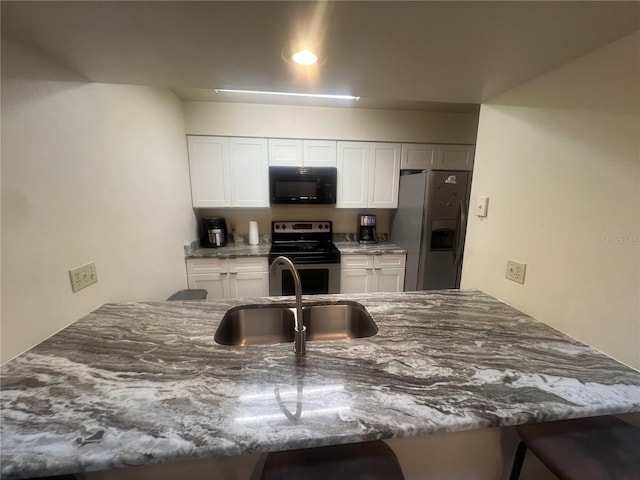 kitchen featuring a peninsula, a kitchen breakfast bar, a sink, stone counters, and stainless steel appliances