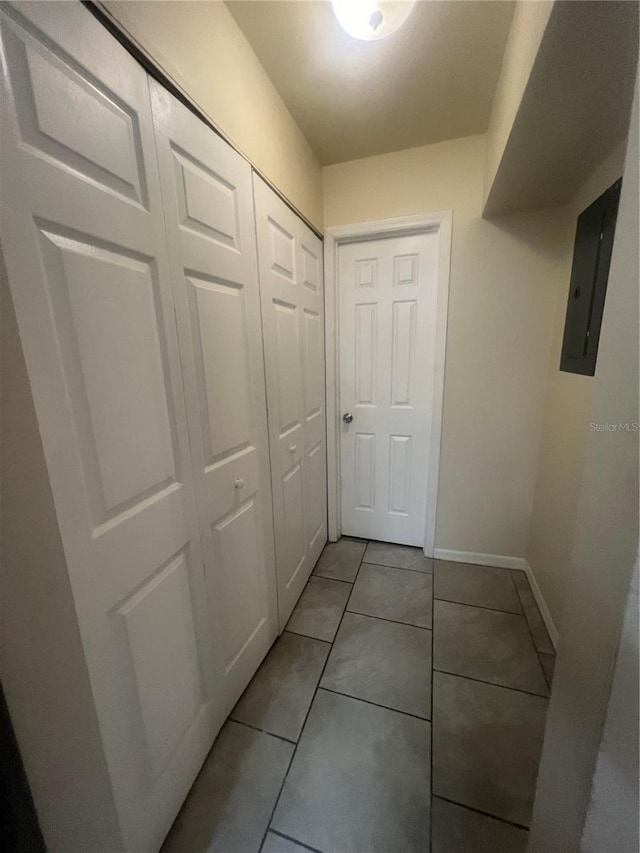 hallway with baseboards, light tile patterned flooring, and electric panel