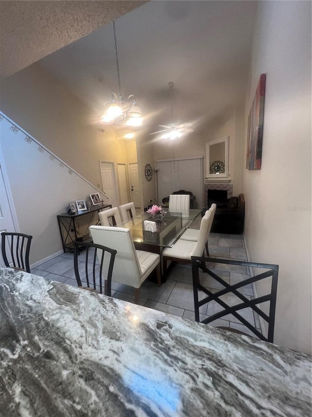 tiled dining area with a fireplace and ceiling fan with notable chandelier