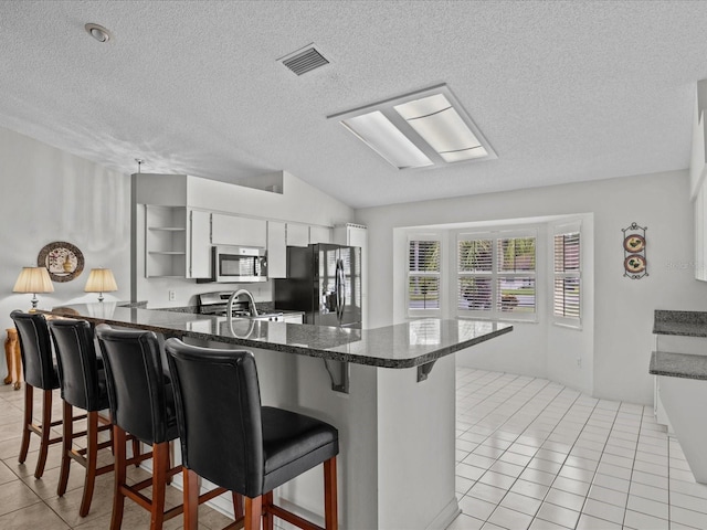 kitchen with appliances with stainless steel finishes, light tile patterned flooring, kitchen peninsula, and a kitchen bar