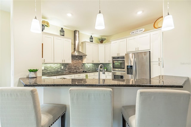 kitchen featuring wall chimney exhaust hood, decorative light fixtures, white cabinetry, appliances with stainless steel finishes, and tasteful backsplash