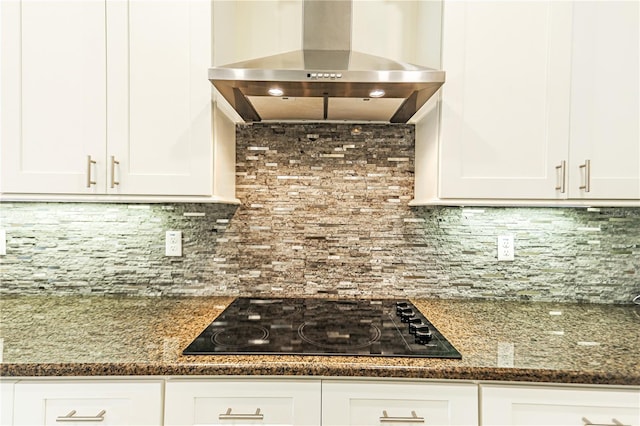 kitchen featuring tasteful backsplash, white cabinetry, dark stone counters, wall chimney exhaust hood, and black cooktop