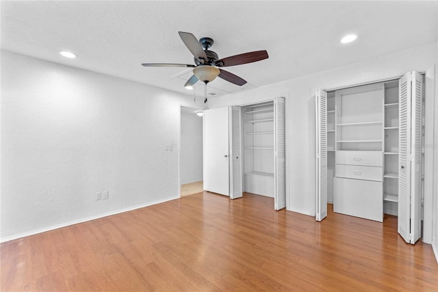 unfurnished bedroom featuring a textured ceiling, wood-type flooring, ceiling fan, and two closets