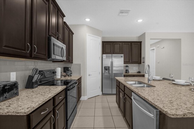 kitchen with sink, a kitchen island with sink, decorative backsplash, light tile patterned floors, and appliances with stainless steel finishes