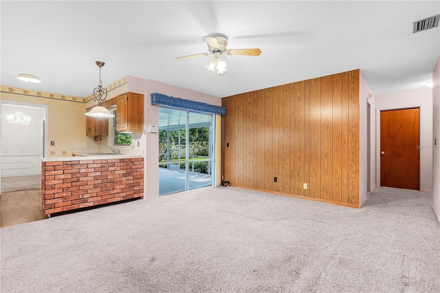 unfurnished living room featuring ceiling fan, wooden walls, sink, and carpet