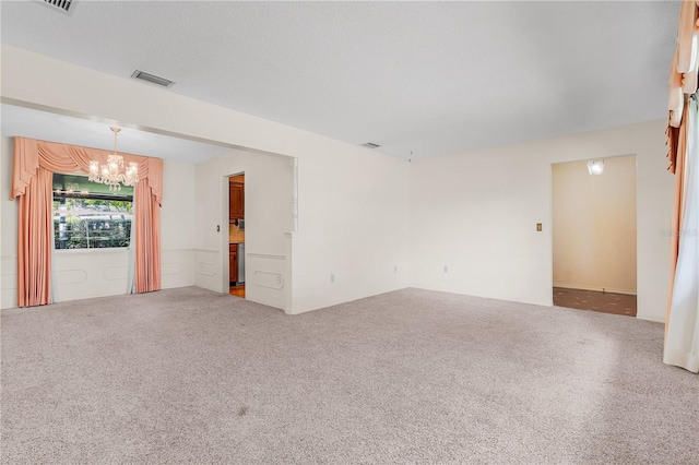 carpeted empty room featuring a textured ceiling and a chandelier