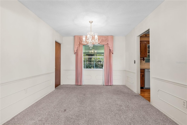 unfurnished room with carpet floors, a textured ceiling, and an inviting chandelier